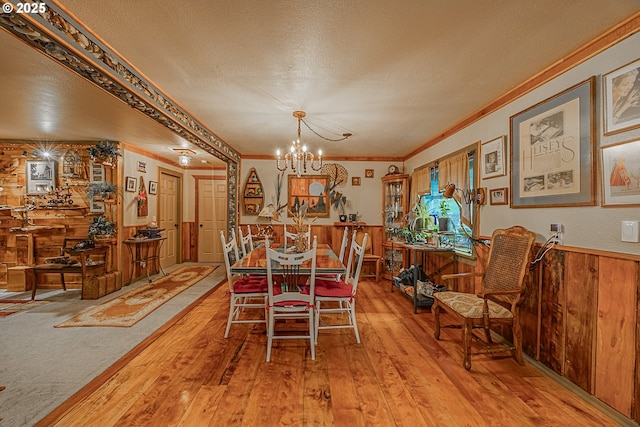 dining space with wood walls, wood-type flooring, a notable chandelier, crown molding, and a textured ceiling