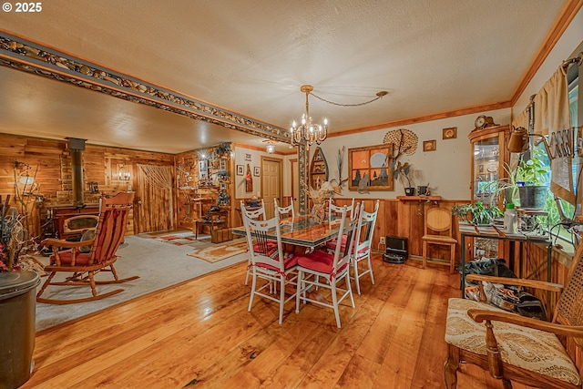 dining area featuring wood walls, a wood stove, a notable chandelier, a textured ceiling, and light hardwood / wood-style flooring