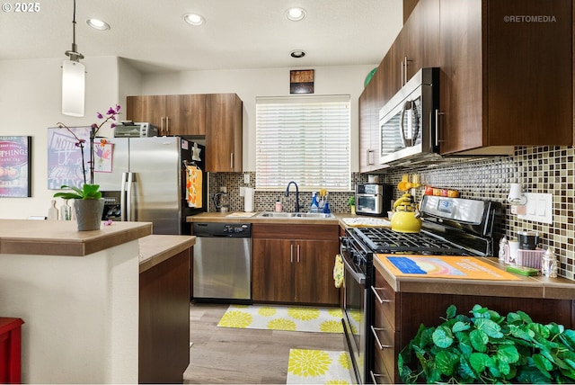 7869 NE Rockne Way, Hillsboro, OR 97006 - kitchen featuring appliances with stainless steel finishes, light countertops, light wood-style floors, backsplash, and hanging light fixtures