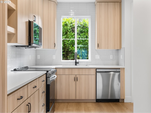 kitchen with appliances with stainless steel finishes, light brown cabinetry, sink, decorative backsplash, and light hardwood / wood-style flooring