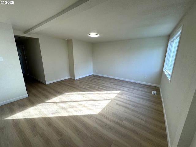 empty room with wood finished floors, visible vents, and baseboards