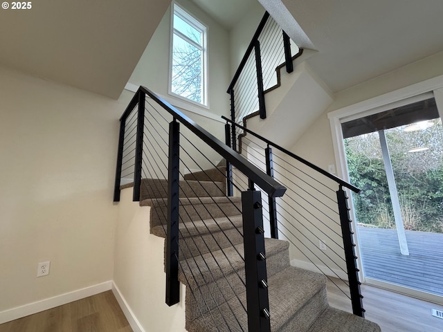 staircase with a wealth of natural light, a high ceiling, baseboards, and wood finished floors