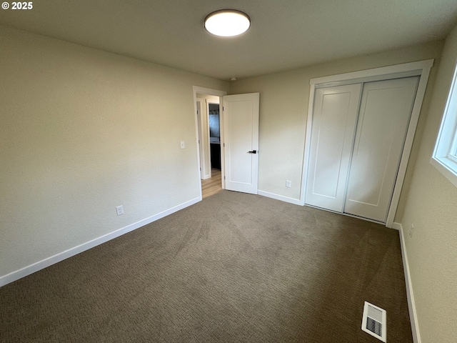 unfurnished bedroom featuring a closet, visible vents, dark carpet, and baseboards