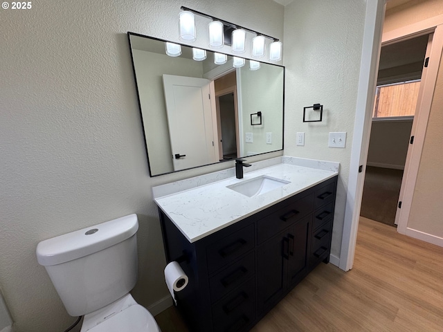 bathroom with a textured wall, vanity, wood finished floors, and toilet