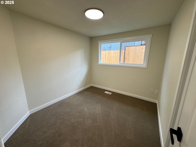 unfurnished room featuring dark colored carpet, visible vents, a textured wall, and baseboards