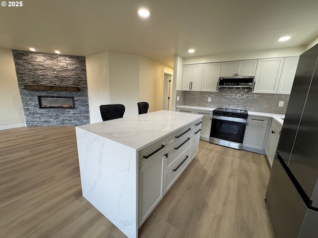 kitchen with stainless steel appliances, light wood-type flooring, a stone fireplace, and tasteful backsplash