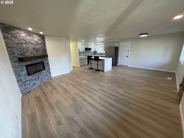 unfurnished living room featuring recessed lighting, light wood-style flooring, a stone fireplace, a textured ceiling, and baseboards