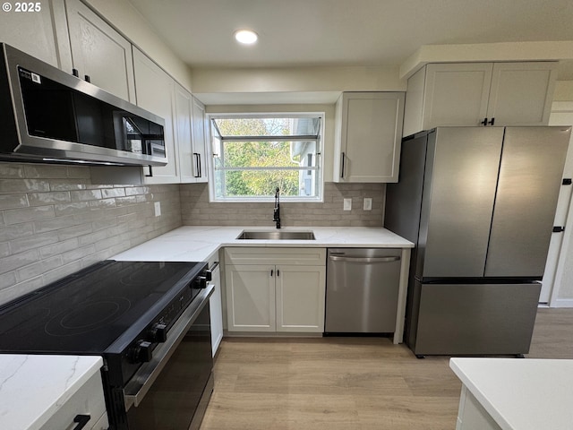 kitchen featuring stainless steel appliances, tasteful backsplash, a sink, and light wood-style floors