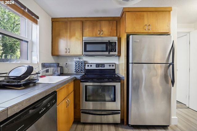 kitchen with dark countertops, decorative backsplash, appliances with stainless steel finishes, a sink, and light wood-type flooring