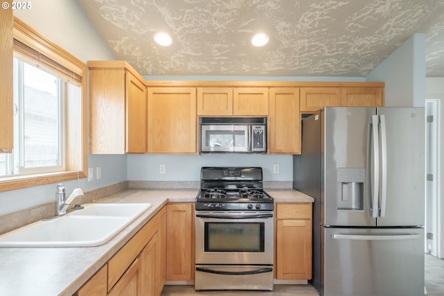 kitchen with a sink, stainless steel appliances, light brown cabinetry, and light countertops