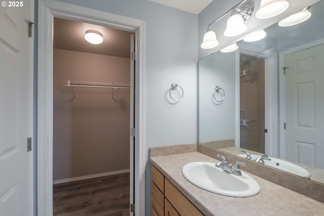 bathroom with wood finished floors, a walk in closet, vanity, and baseboards