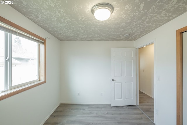 empty room featuring light wood finished floors, baseboards, and a textured ceiling