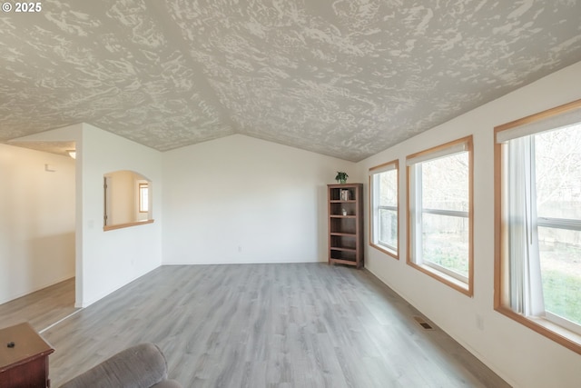 unfurnished living room featuring plenty of natural light, light wood-style flooring, visible vents, and vaulted ceiling