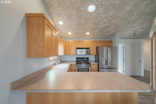 kitchen featuring stainless steel appliances, light brown cabinetry, a peninsula, and a sink