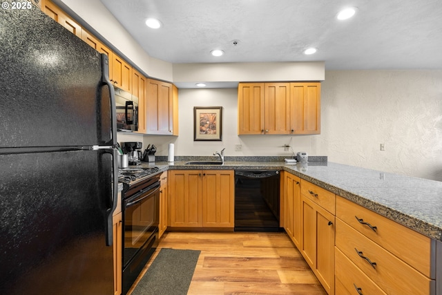 kitchen with sink, black appliances, light hardwood / wood-style floors, and light stone countertops