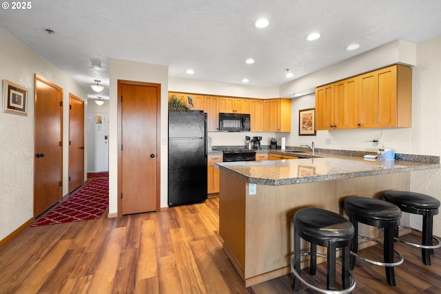 kitchen with a breakfast bar area, light hardwood / wood-style flooring, kitchen peninsula, and black appliances