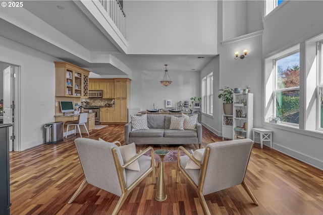 living room with built in study area, a high ceiling, baseboards, and dark wood-style flooring