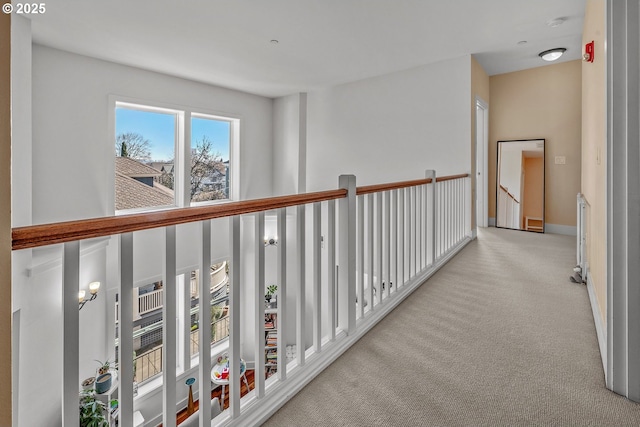 hall featuring baseboards, an upstairs landing, and carpet flooring