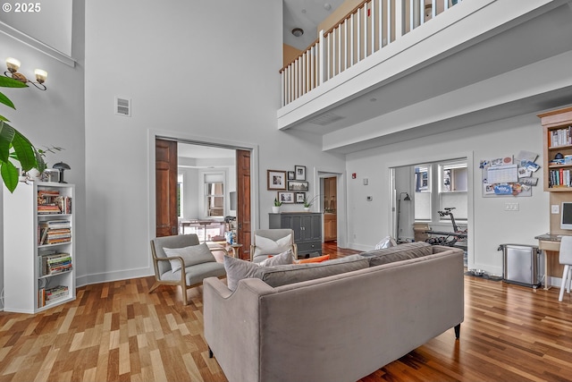 living area with light wood-type flooring, visible vents, baseboards, and a towering ceiling