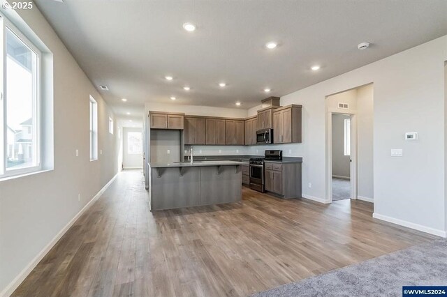 kitchen with a center island with sink, light wood-style flooring, appliances with stainless steel finishes, open floor plan, and recessed lighting