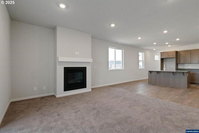 unfurnished living room with light carpet, recessed lighting, a sink, and a glass covered fireplace