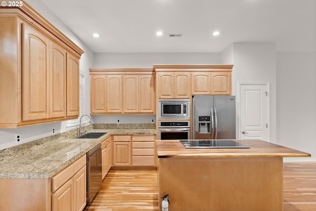 kitchen with appliances with stainless steel finishes, light brown cabinetry, sink, and a kitchen island