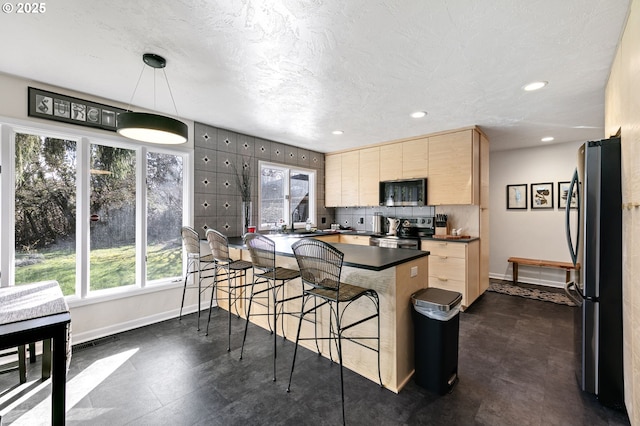 kitchen with dark countertops, plenty of natural light, a kitchen bar, and appliances with stainless steel finishes