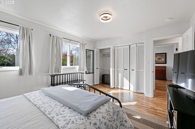 bedroom with multiple closets, light wood-style flooring, and baseboards