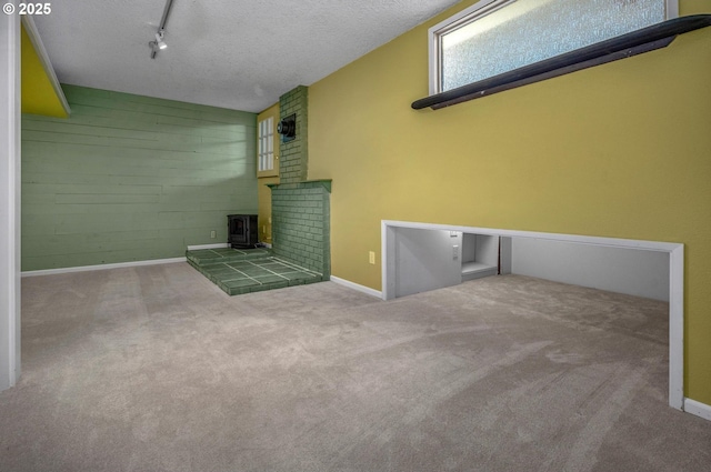 32813 NW Peak Rd, Scappoose, OR 97056 - unfurnished living room featuring a wood stove, baseboards, carpet flooring, wooden walls, and rail lighting