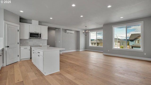 kitchen with white cabinets, a kitchen island, a wall mounted air conditioner, and hanging light fixtures