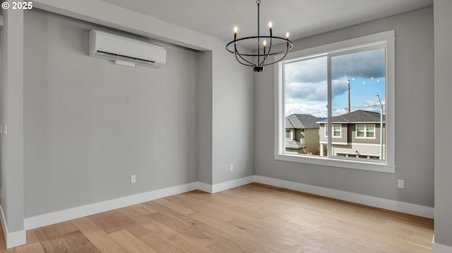 spare room featuring light wood-type flooring, an AC wall unit, and a notable chandelier