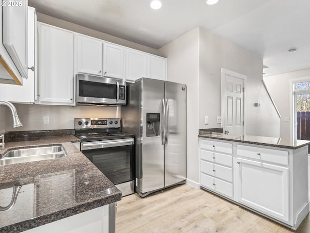 kitchen with white cabinetry, appliances with stainless steel finishes, sink, and dark stone countertops