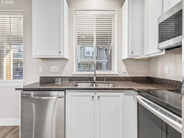 kitchen with sink, dark stone countertops, appliances with stainless steel finishes, hardwood / wood-style flooring, and white cabinets