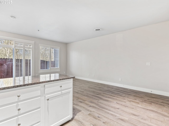 interior space with white cabinetry, light hardwood / wood-style flooring, and dark stone counters