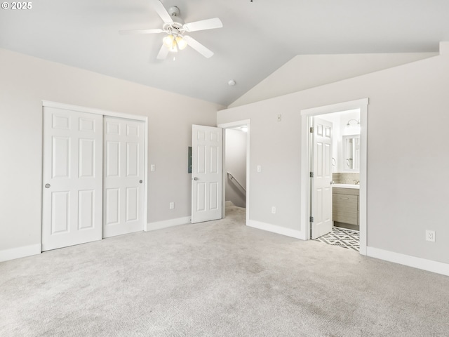 unfurnished bedroom featuring ceiling fan, connected bathroom, light carpet, vaulted ceiling, and a closet