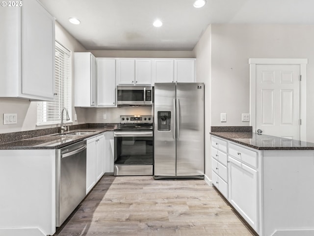 kitchen with appliances with stainless steel finishes, sink, white cabinets, dark stone counters, and light wood-type flooring