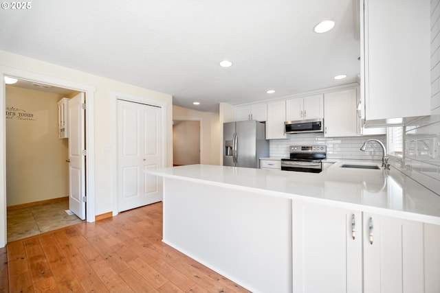1602 NE 16th Ct, Battle Ground, WA 98604 - kitchen featuring stainless steel appliances, a sink, light wood-type flooring, white cabinetry, and a peninsula