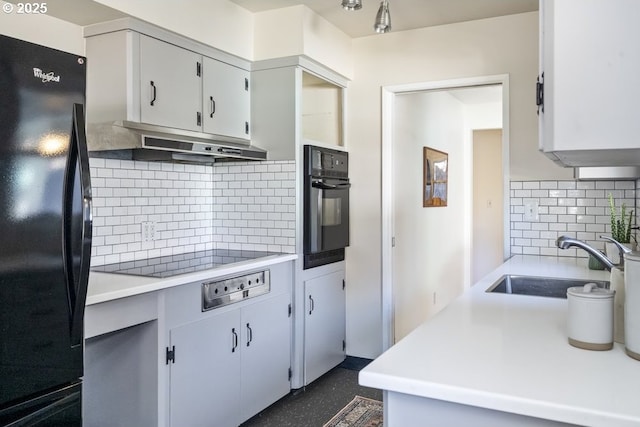 kitchen with black appliances, under cabinet range hood, a sink, light countertops, and decorative backsplash