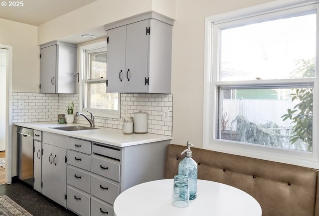 kitchen featuring gray cabinetry, decorative backsplash, light countertops, a sink, and dishwasher