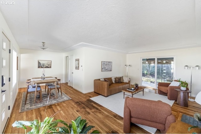 living area with baseboards, light wood-style floors, and a textured ceiling