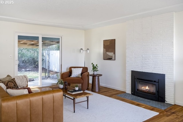 living room featuring a brick fireplace, wood finished floors, and baseboards