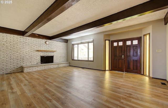 8400 Cason Rd, Gladstone, OR 97027 - unfurnished living room with beam ceiling, light wood-type flooring, a fireplace, a textured ceiling, and brick wall