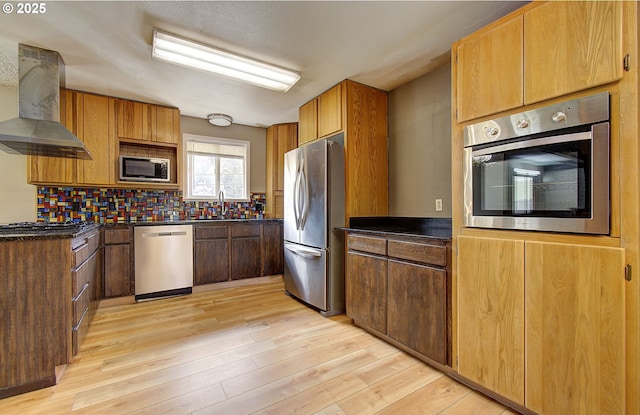 8400 Cason Rd, Gladstone, OR 97027 - kitchen with appliances with stainless steel finishes, wall chimney exhaust hood, dark countertops, light wood-type flooring, and decorative backsplash