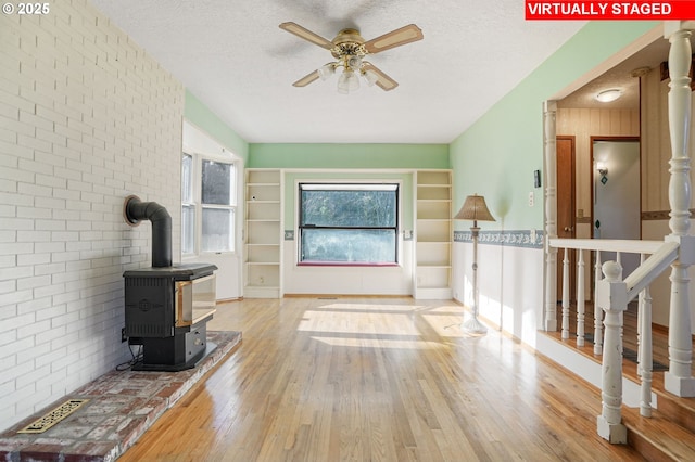 living area featuring a textured ceiling, a wood stove, a ceiling fan, and wood finished floors