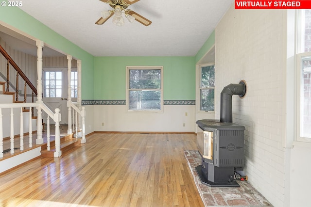 living area with a wood stove, wood finished floors, baseboards, ceiling fan, and stairs