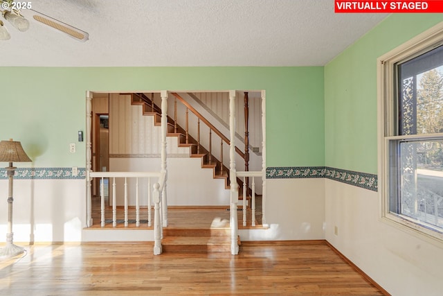 stairs featuring ceiling fan, baseboards, a textured ceiling, and wood finished floors