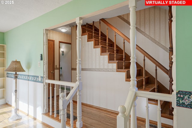 staircase with wallpapered walls, wood finished floors, and a textured ceiling