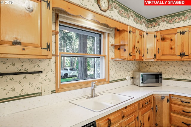 kitchen with brown cabinetry, wallpapered walls, a sink, light countertops, and stainless steel microwave