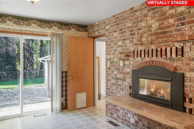 living area featuring tile patterned floors, visible vents, a brick fireplace, and brick wall