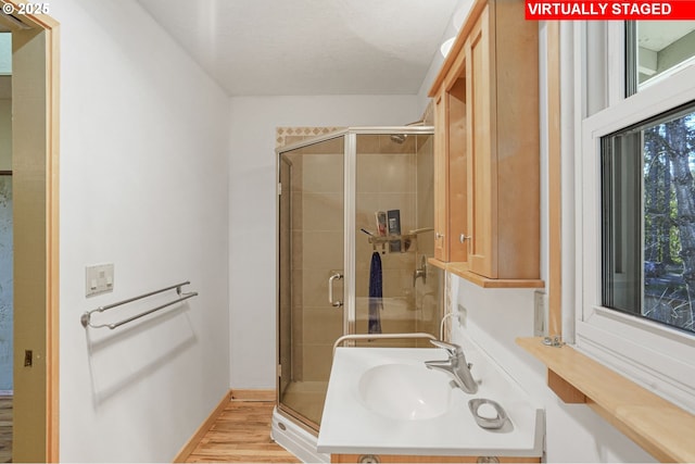 bathroom with a shower stall, wood finished floors, baseboards, and a sink